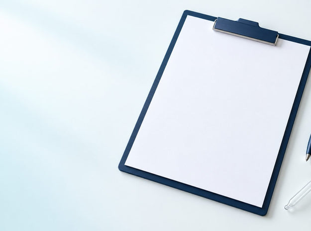 A blank sheet of paper on a navy clipboard with a navy pen and a glass dropper on a white desk